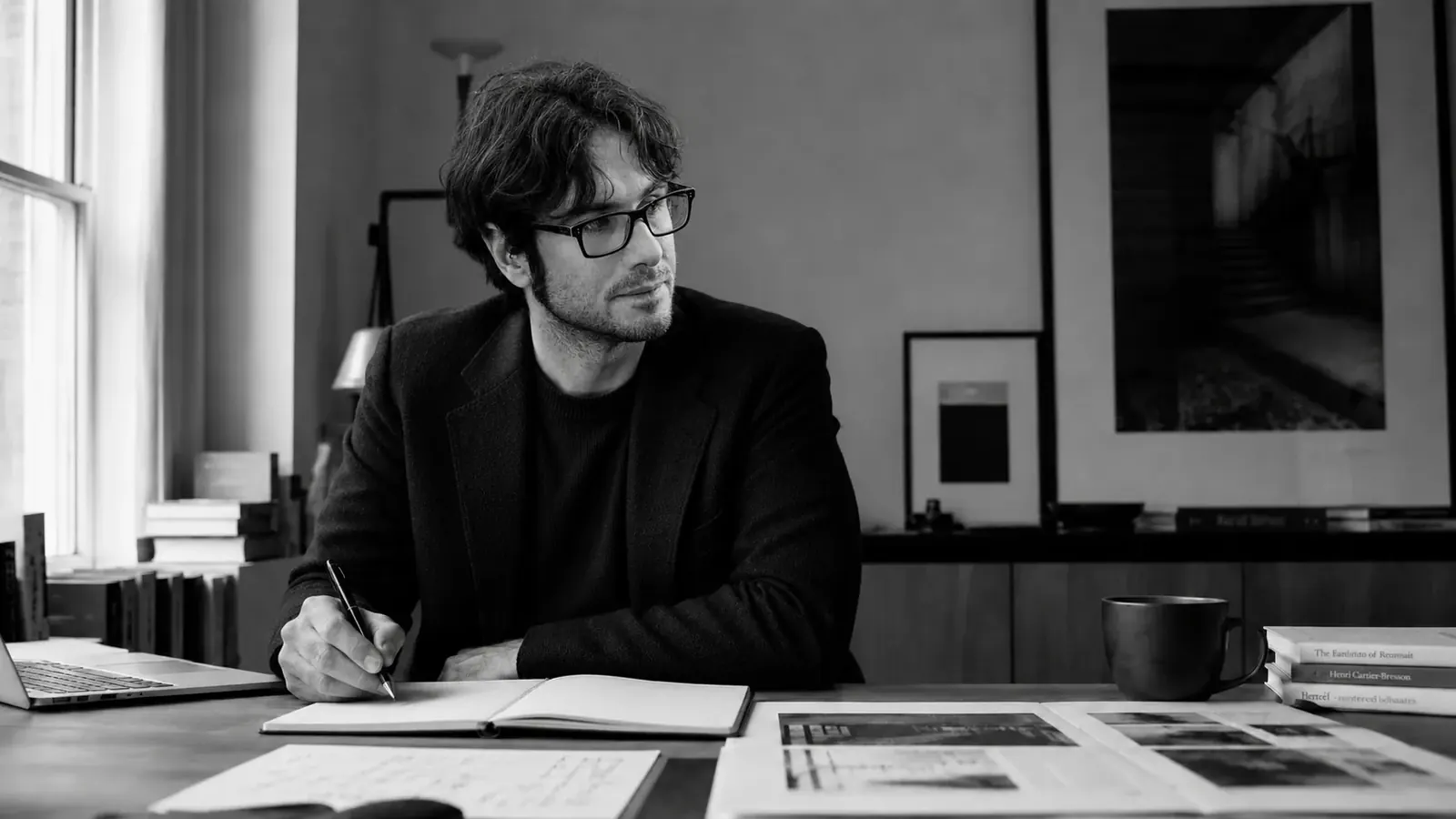 Alessandro Gentili writing at a desk in a black-and-white editorial portrait, representing strategy, writing and systems thinking.