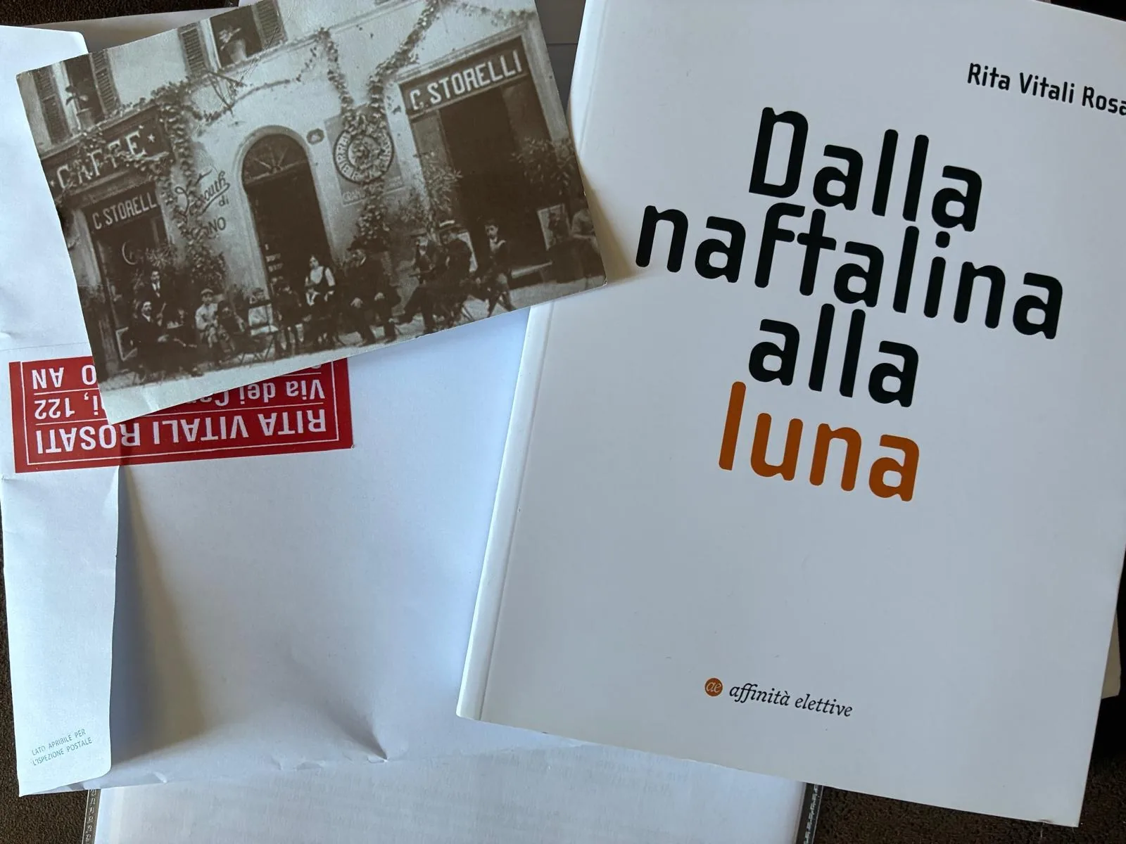 Cartolina storica di un caffè cittadino accanto al libro “Dalla naftalina alla luna” di Rita Vitali Rosati.